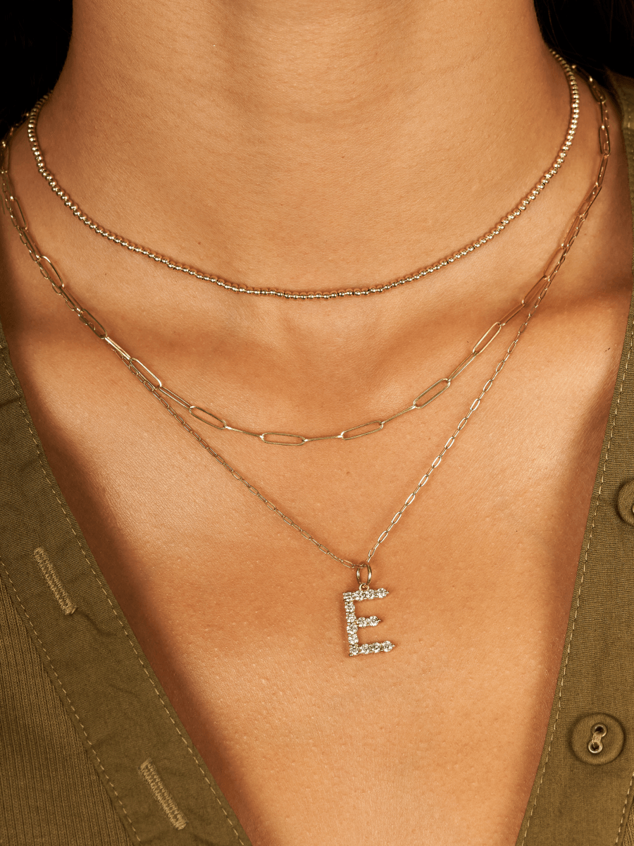 Large 14K gold diamond initial charm on thin and dainty gold paperclip chain layered with gold paperclip necklace and gold beaded choker necklace
