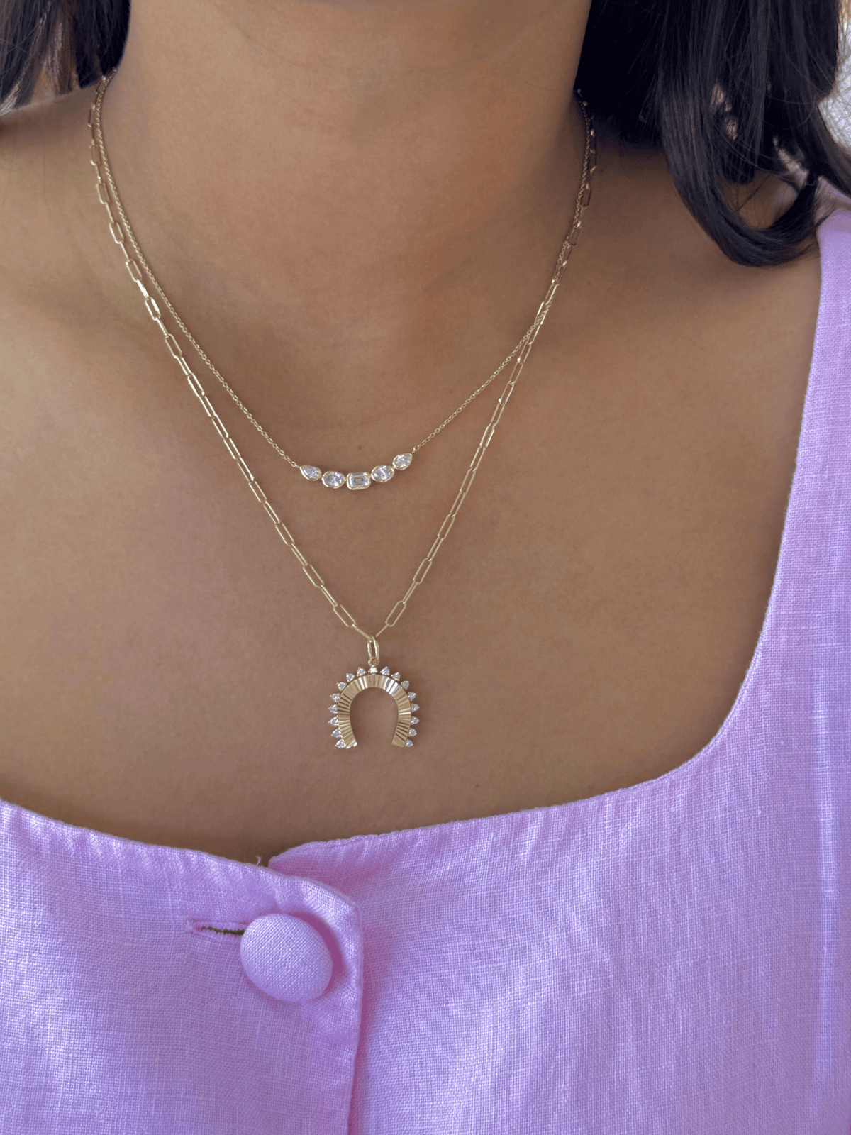 Necklace with a horseshoe pendant worn by a person against a pink background