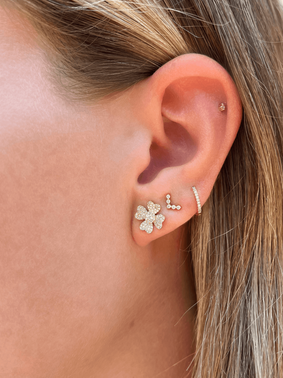 Diamond flower earrings paired with diamond v earrings, diamond huggie, and diamond mini stud on model ear