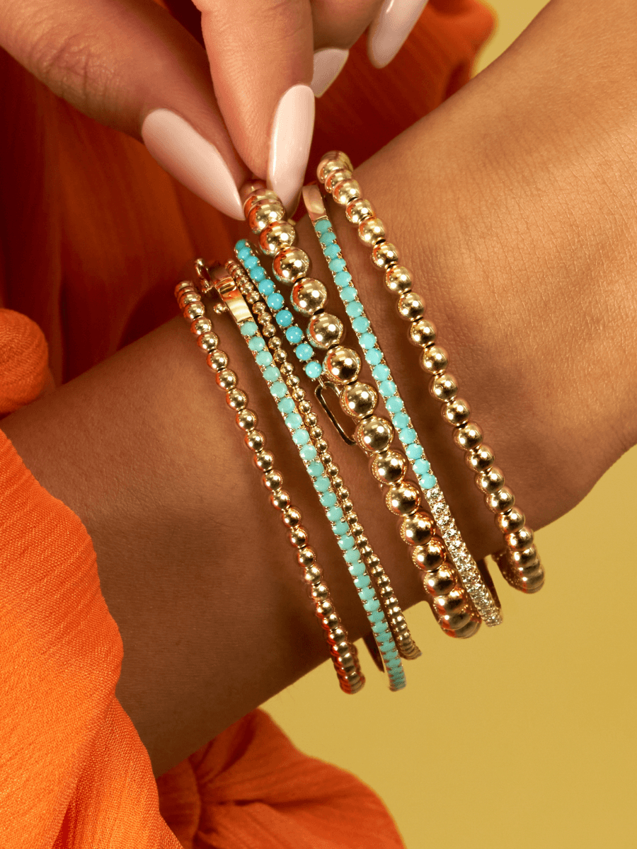 14K yellow gold half paperclip chain half turquoise tennis bracelet layered with gold beaded bracelets, gold turquoise bangle, and gold diamond and turquoise bangle