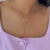 Necklace with a cross pendant worn by a person in a pink top.