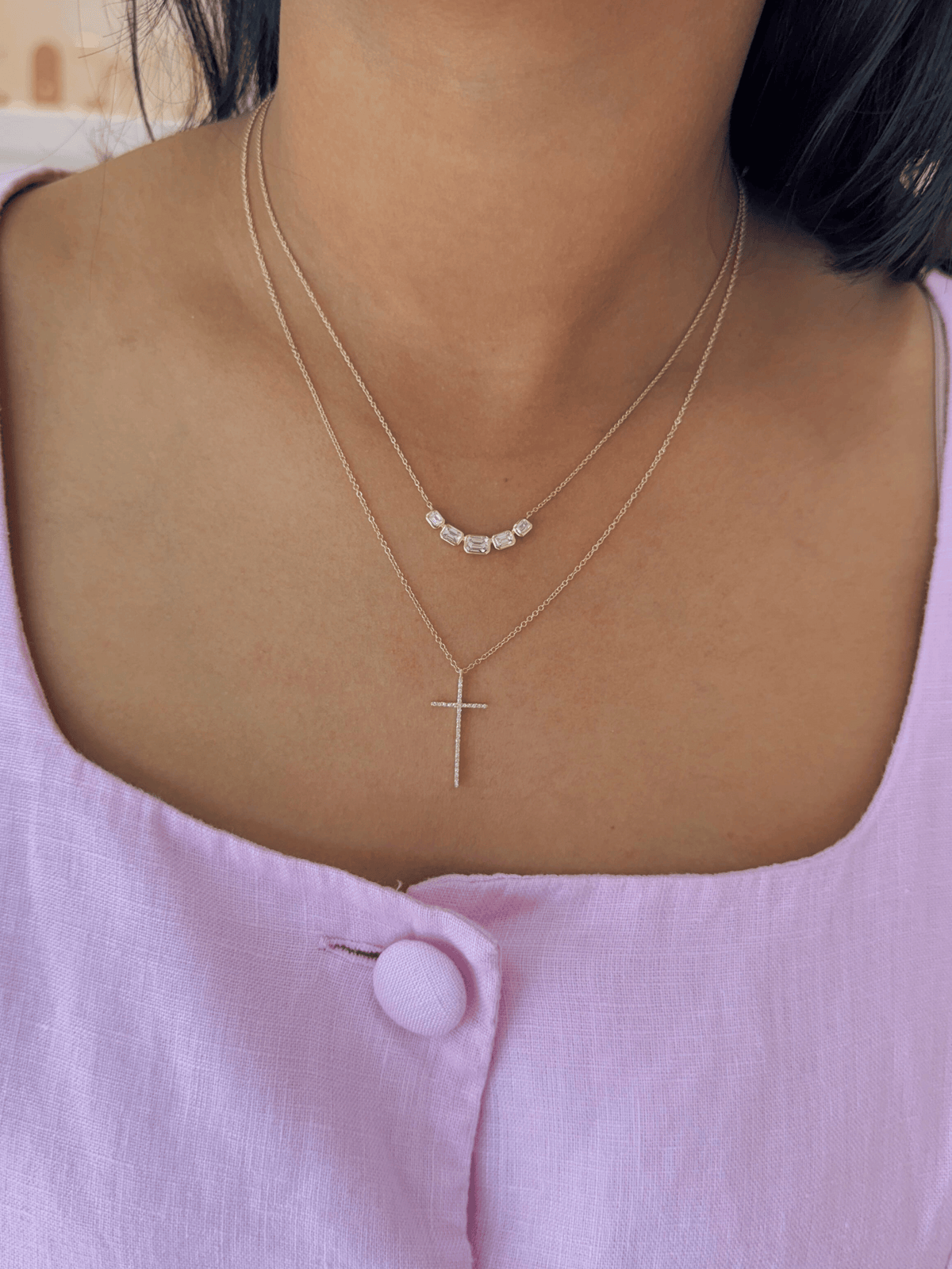 Necklace with a cross pendant worn by a person in a pink top.