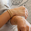 Gold stretch bracelet set 3mm, 4mm, and 5mm on model's left wrist and gold chain bracelets on model's right wrist