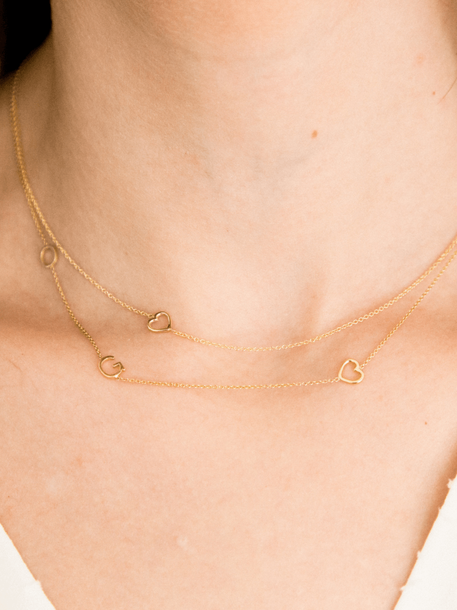 Dainty gold chain with initials and gold heart charm layered with another dainty gold chain with singular gold heart charm 