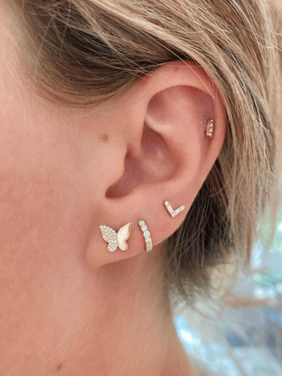 Pave diamond butterfly earring paired with diamond huggie, chevron earring, and diamond bar stud on model ear