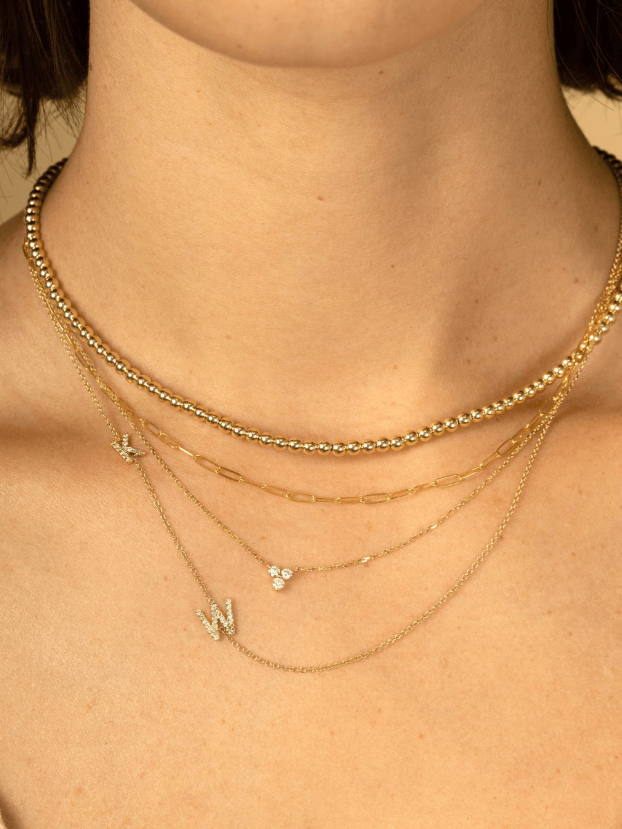 Gold beaded choker layered with thin gold paperclip necklace, diamond trio necklace, and diamond initial necklace