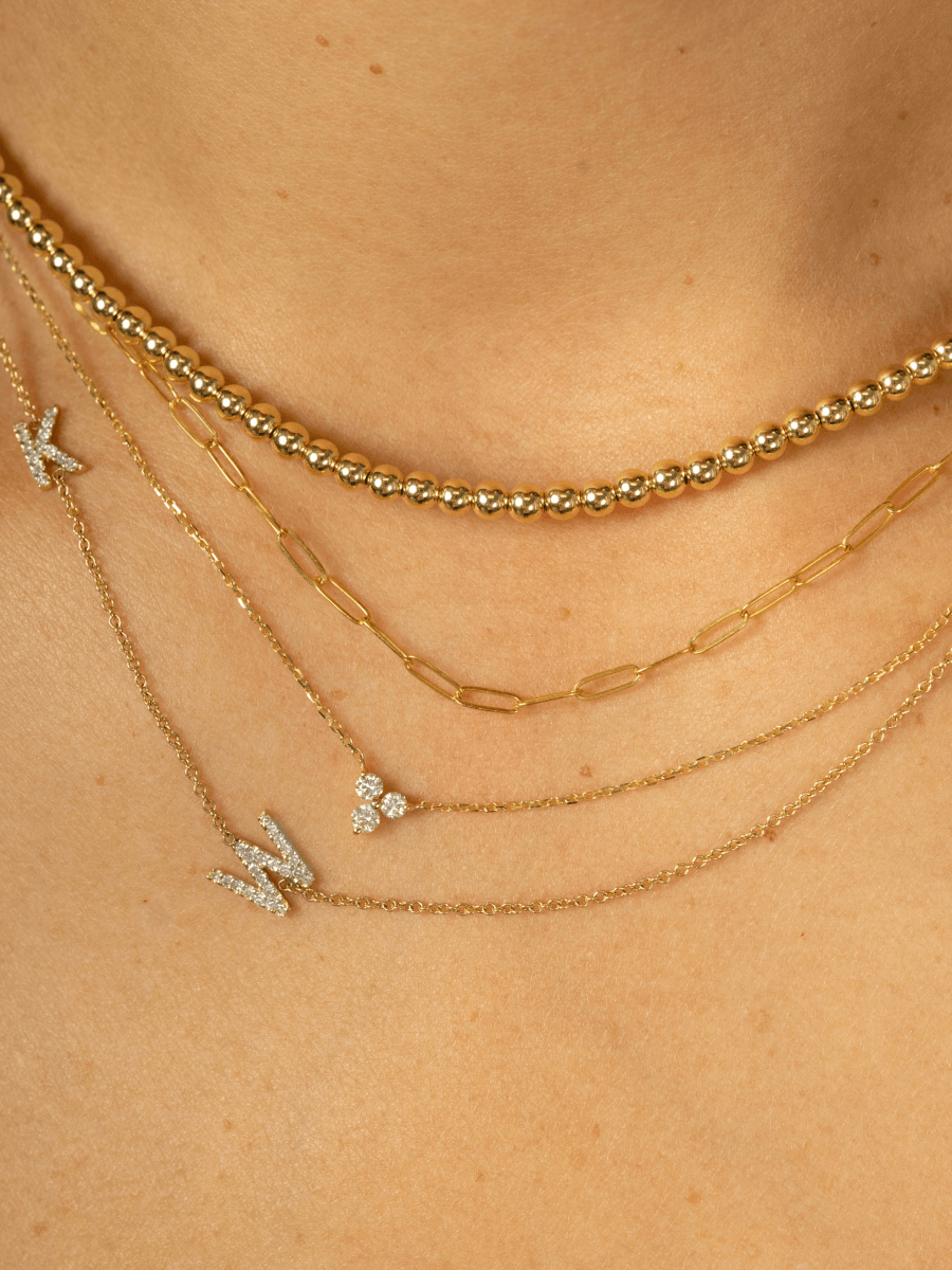 Gold beaded choker layered with thin gold paperclip necklace, diamond trio necklace, and diamond initial necklace