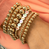 Name bracelet with gold beads paired with simple gold beaded stretchy bracelets on model wrist