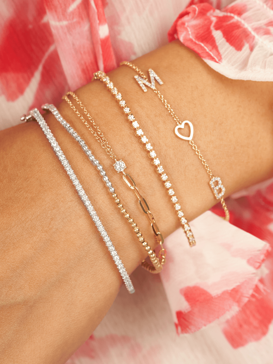 Bezeled diamond tennis chain bracelet stacked with diamond initial bracelet, silver and gold beaded bracelets, diamond tennis bracelet, and bracelet with half paperclip chain half dainty chain with single diamond