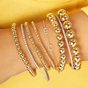 Gold beaded bracelets paired with diamond cuff, diamond tennis bracelet, and diamond initial bracelet on model wrist