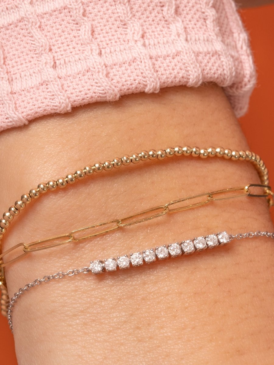 2mm gold beaded bracelet stacked with gold paperclip chain bracelet and diamond tennis chain bracelet on model wrist