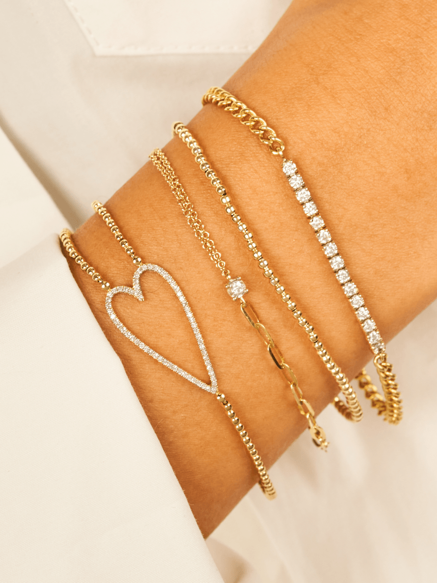 2mm gold stretch bracelet stacked with diamond tennis chain bracelet, mixed chain and diamond bracelet, and diamond open heart bracelet on model wrist