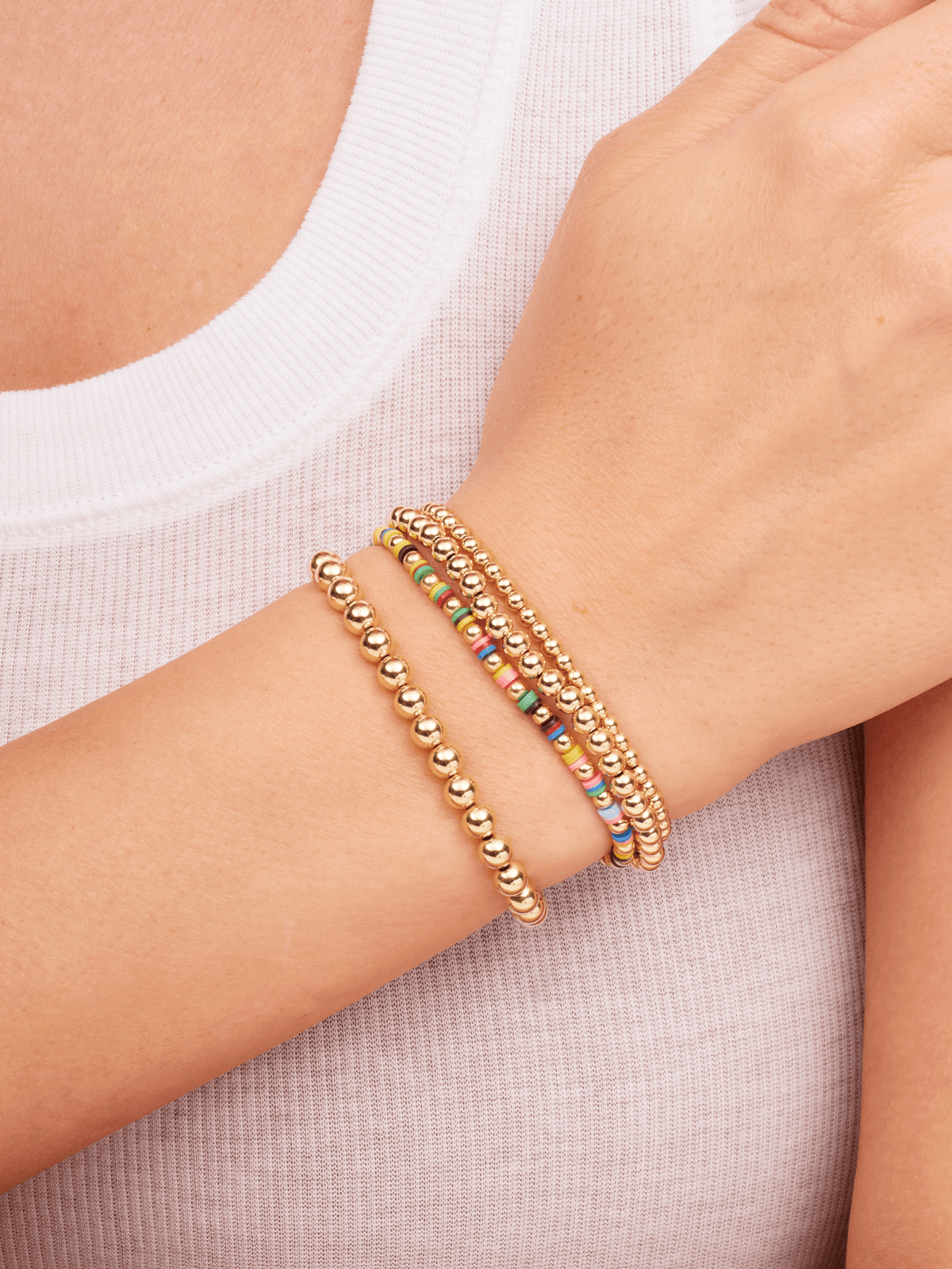 Gold bead stretch bracelets paired with colorful beaded stretch bracelet on model wrist