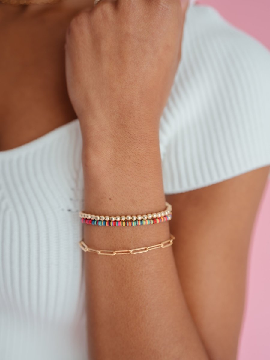 Gold beaded stretch bracelet paired with colorful stretch bracelet and gold paperclip bracelet on model wrist