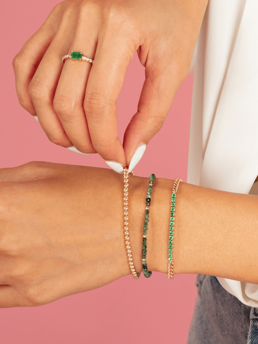 Small gold bead stretch bracelet paired with emerald and gold beaded stretch bracelet and emerald tennis chain bracelet on model wrist