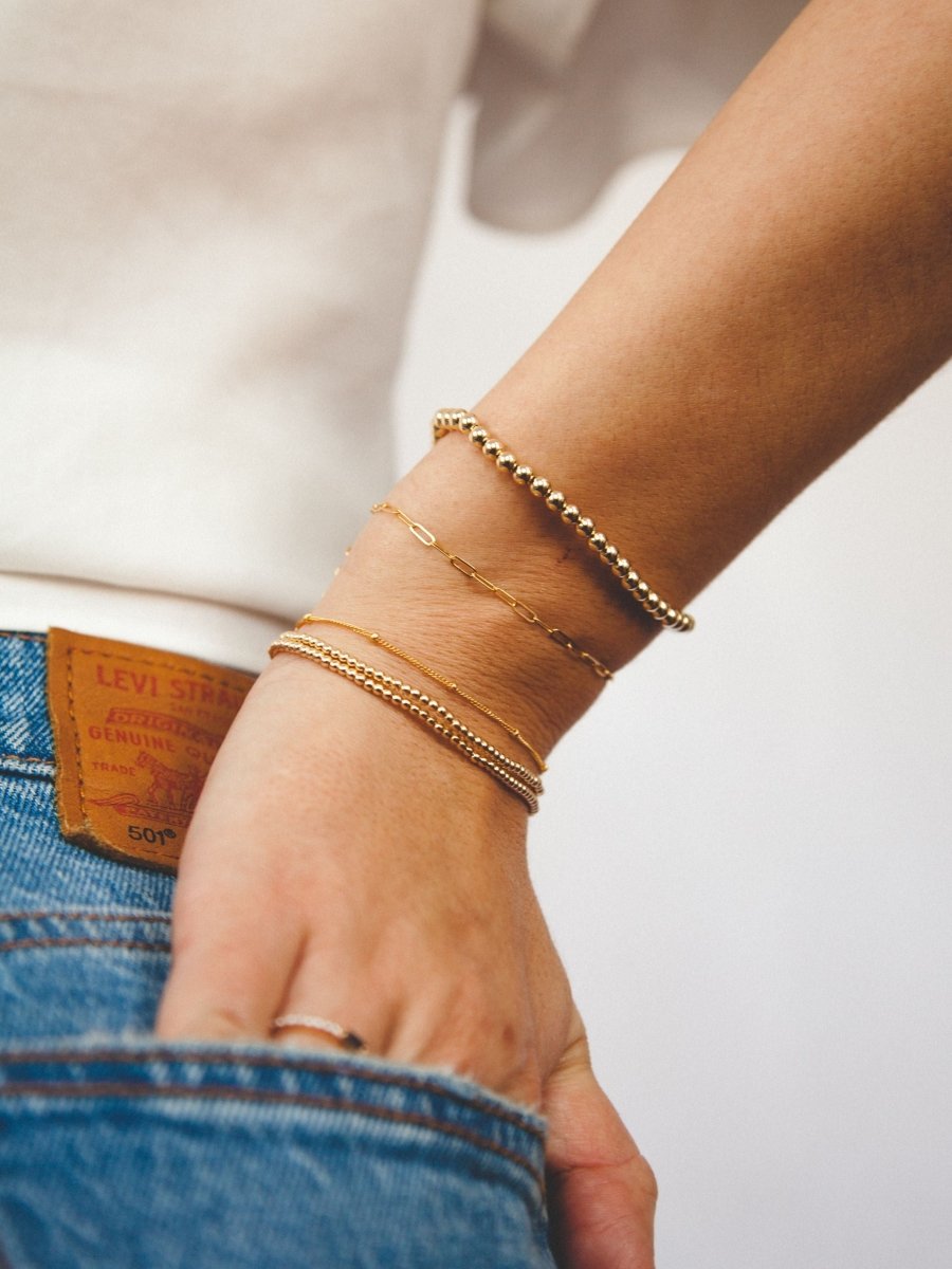 Gold beaded stretch bracelets paired with gold paperclip bracelet and gold satellite chain bracelet on model wrist
