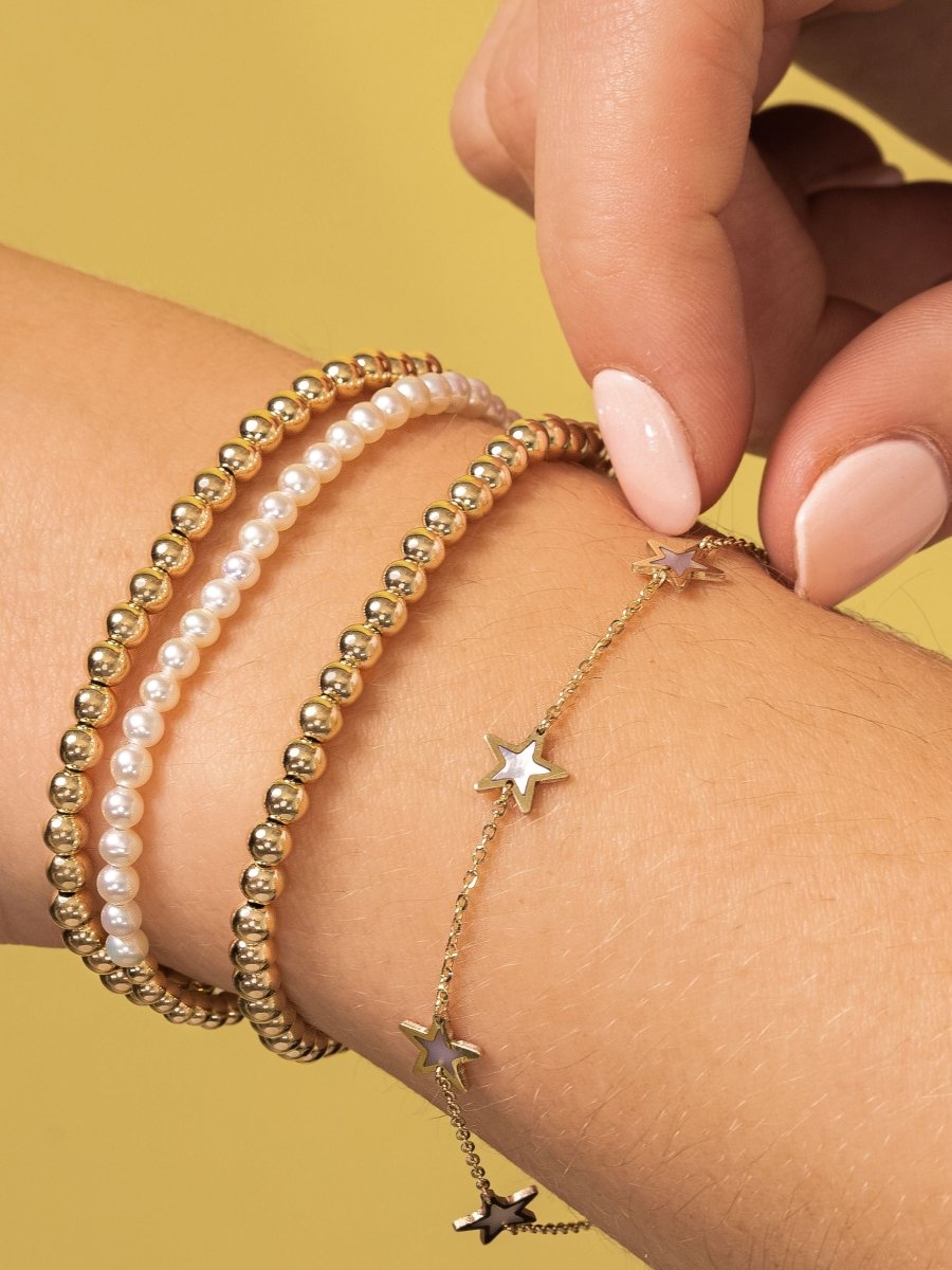 Gold beaded stretch bracelets paired with pearl stretch bracelet and mother of pearl star bracelet on model wrist