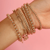 Gold beaded bracelets stacked with chunky gold bracelet, large paperclip bracelet, and diamond initial bracelet on model wrist