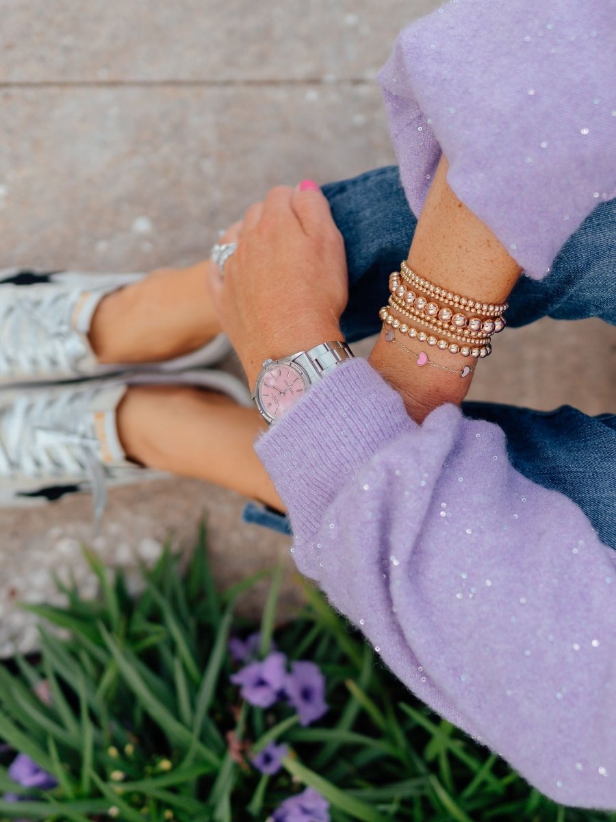 Gold beaded stretch bracelets paired with pink and white enamel heart bracelet on model wrist