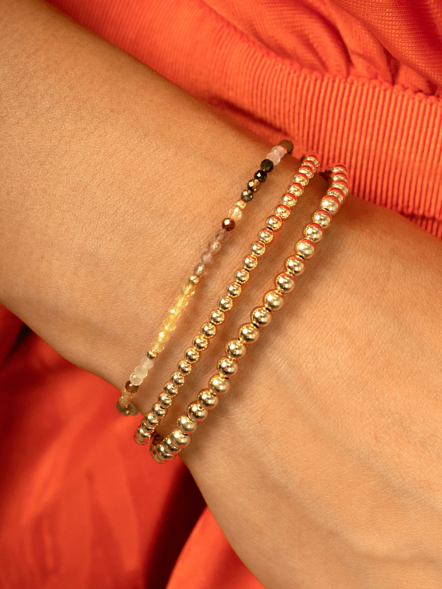Stackable beaded stretch bracelets yellow gold 3mm and 4mm paired with rainbow tourmaline stretch bracelet on model wrist