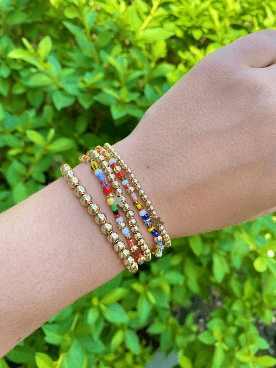 Rainbow bracelets with gold cross charms [paired with gold beaded stretchy bracelets on model wrist