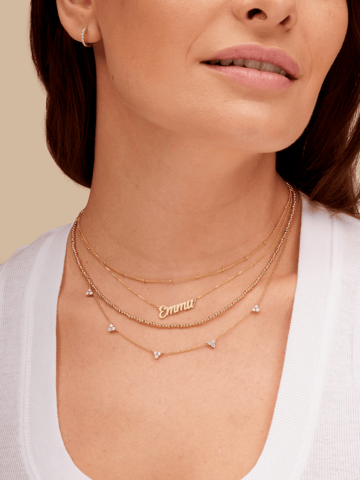 14K gold script name necklace layered with gold beaded necklace, trio triangle diamond necklace, and gold satellite chain