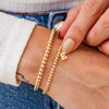 Initial bracelet with gold beads and gold charm paired with simple gold beaded bracelet on model wrist