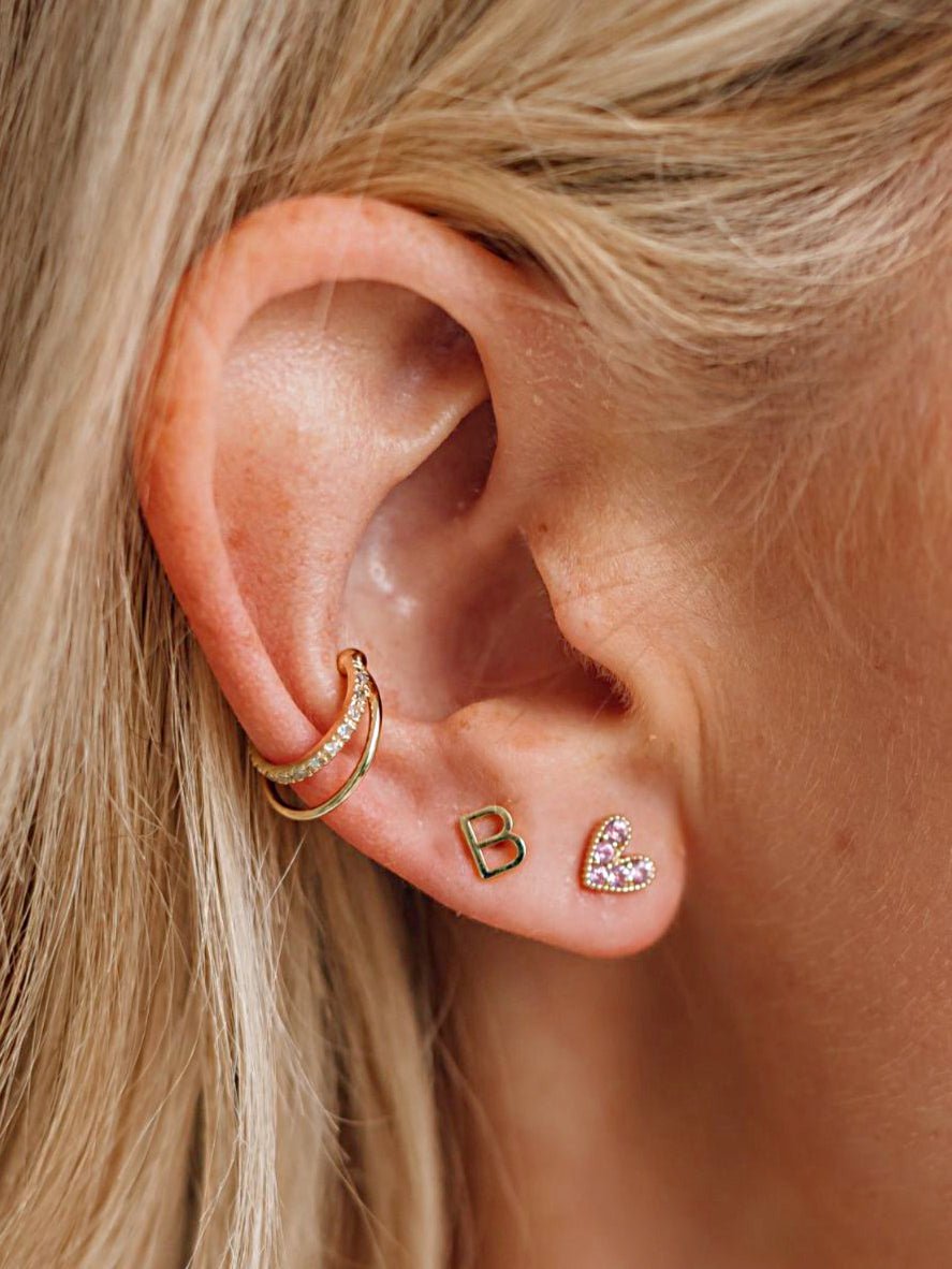 Pink sapphire heart stud paired with gold initial stud and diamond and gold cuff on model ear