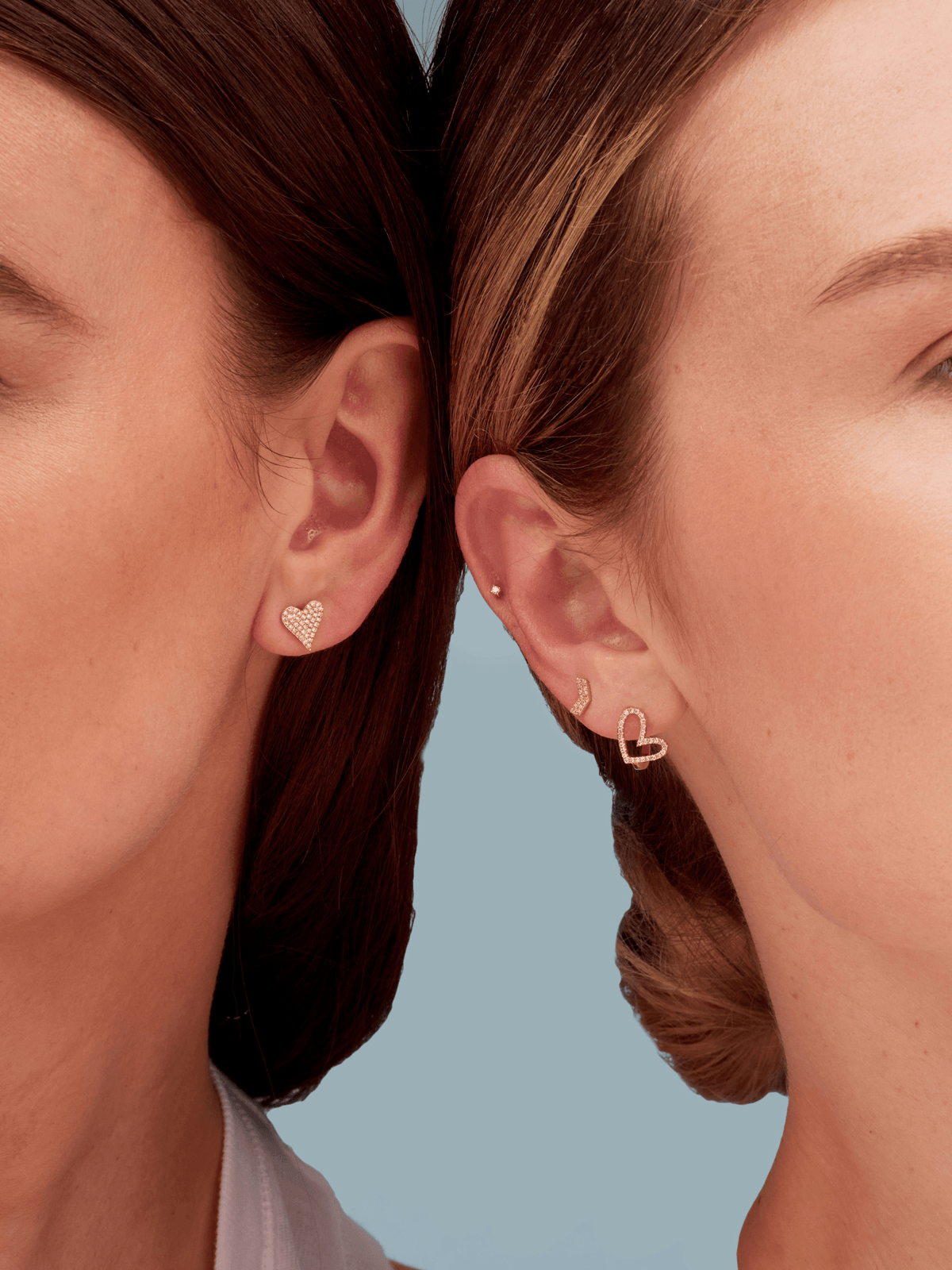 Diamond heart earring on left model's ear and diamond heart huggie paired with chevron stud and diamond stud on right model's ear