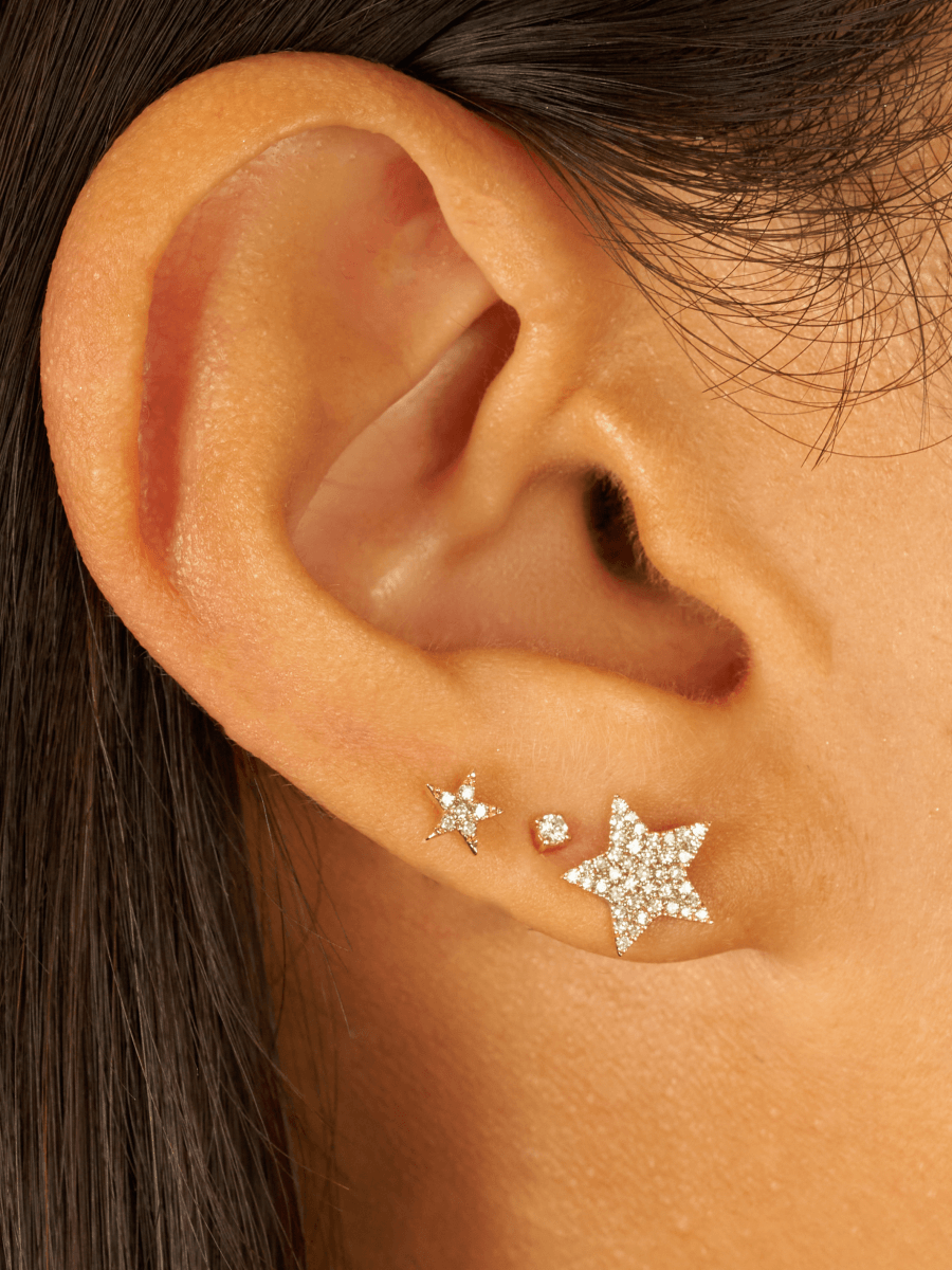 Mini gold star earring with diamond paired with diamond stud and larger gold star earring on model ear