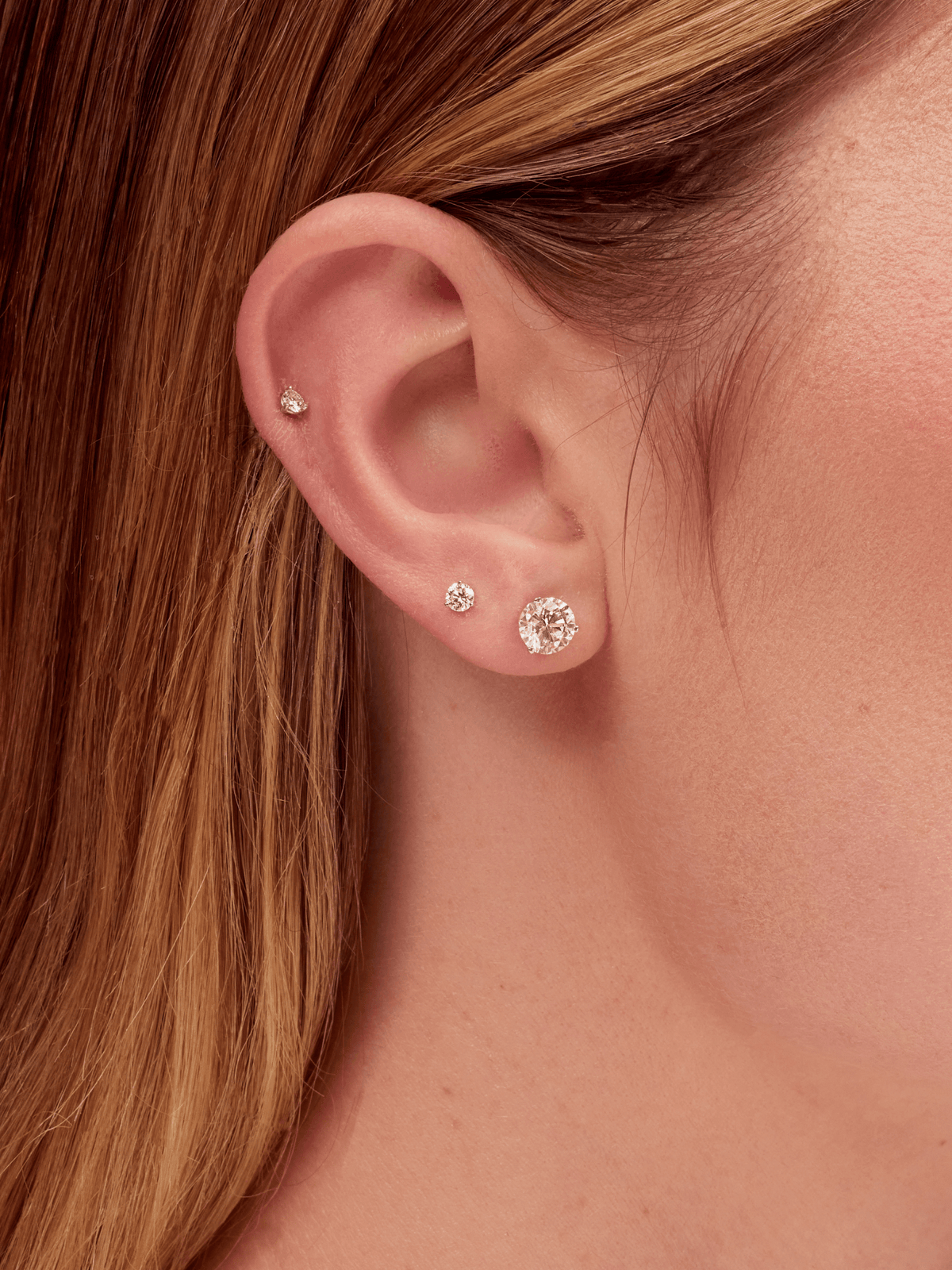 Three diamond stud earrings on model ear