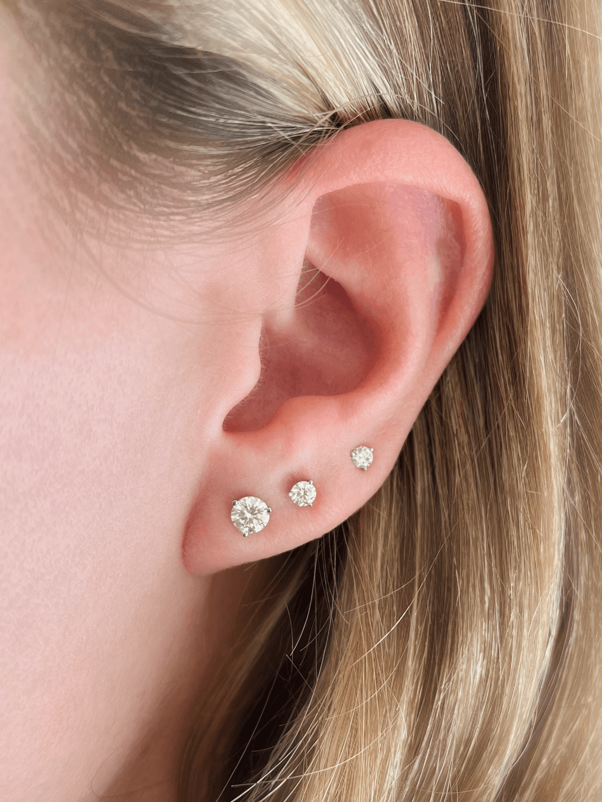 Three diamond stud earrings in different sizes on model ear