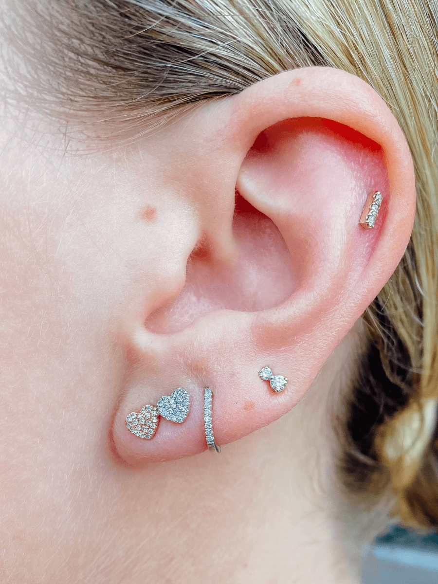 Diamond heart earring paired with diamond huggie, double diamond stud, and diamond bar stud on model ear