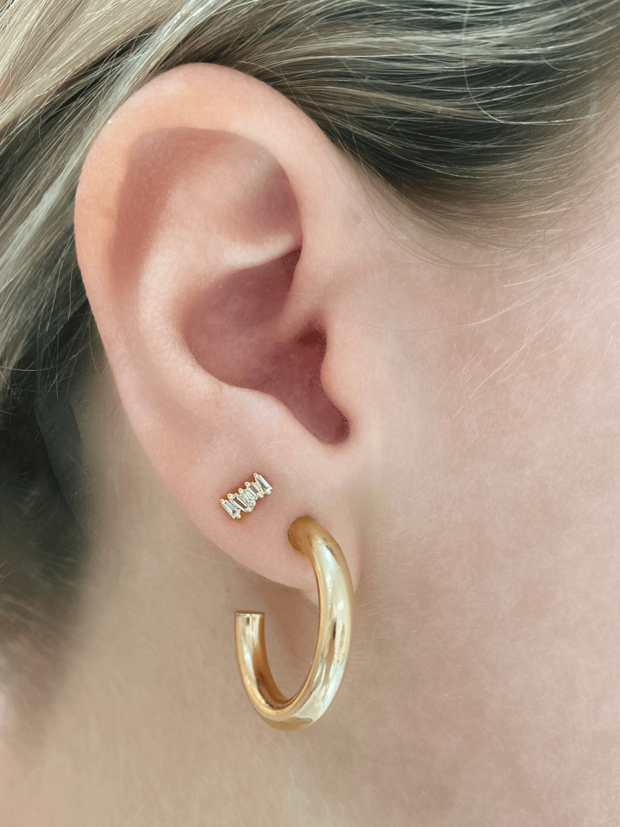 Baguette diamond stud earring paired with chunky gold hoop on model ear