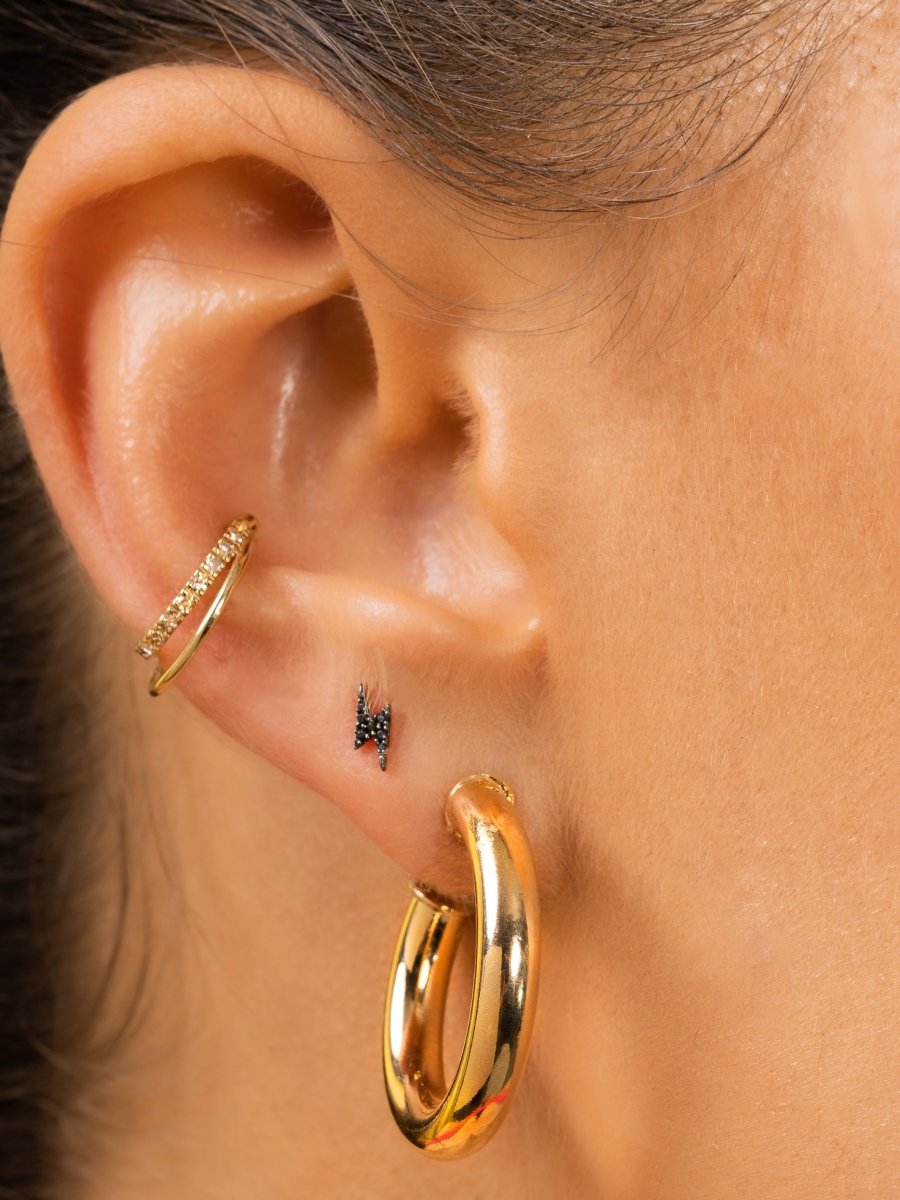 Chunky gold hoop paired with black diamond lightning bolt stud and gold and diamond ear cuff on model ear
