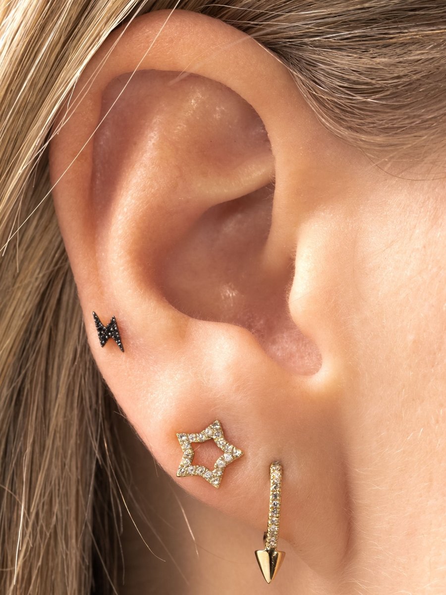Diamond huggie with spike paired with diamond open star stud and black diamond lightning bolt stud on model ear