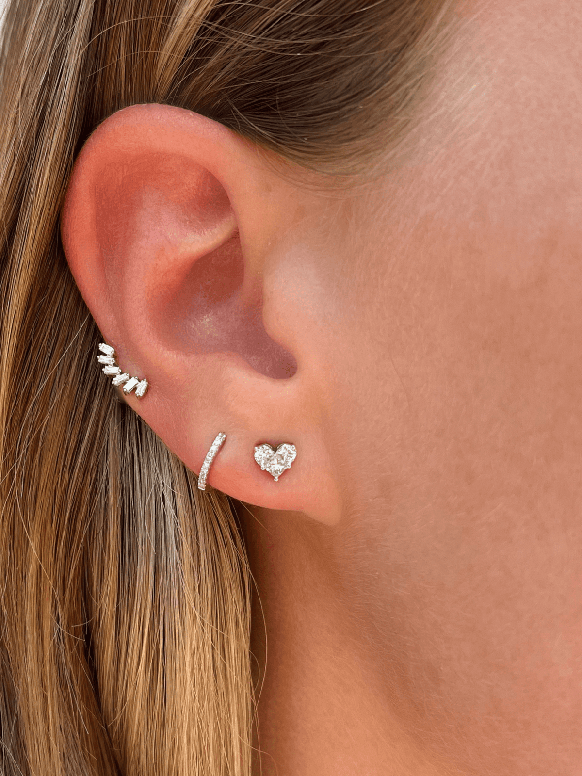 Baguette diamond earrings paired with diamond huggie and diamond illusion heart stud