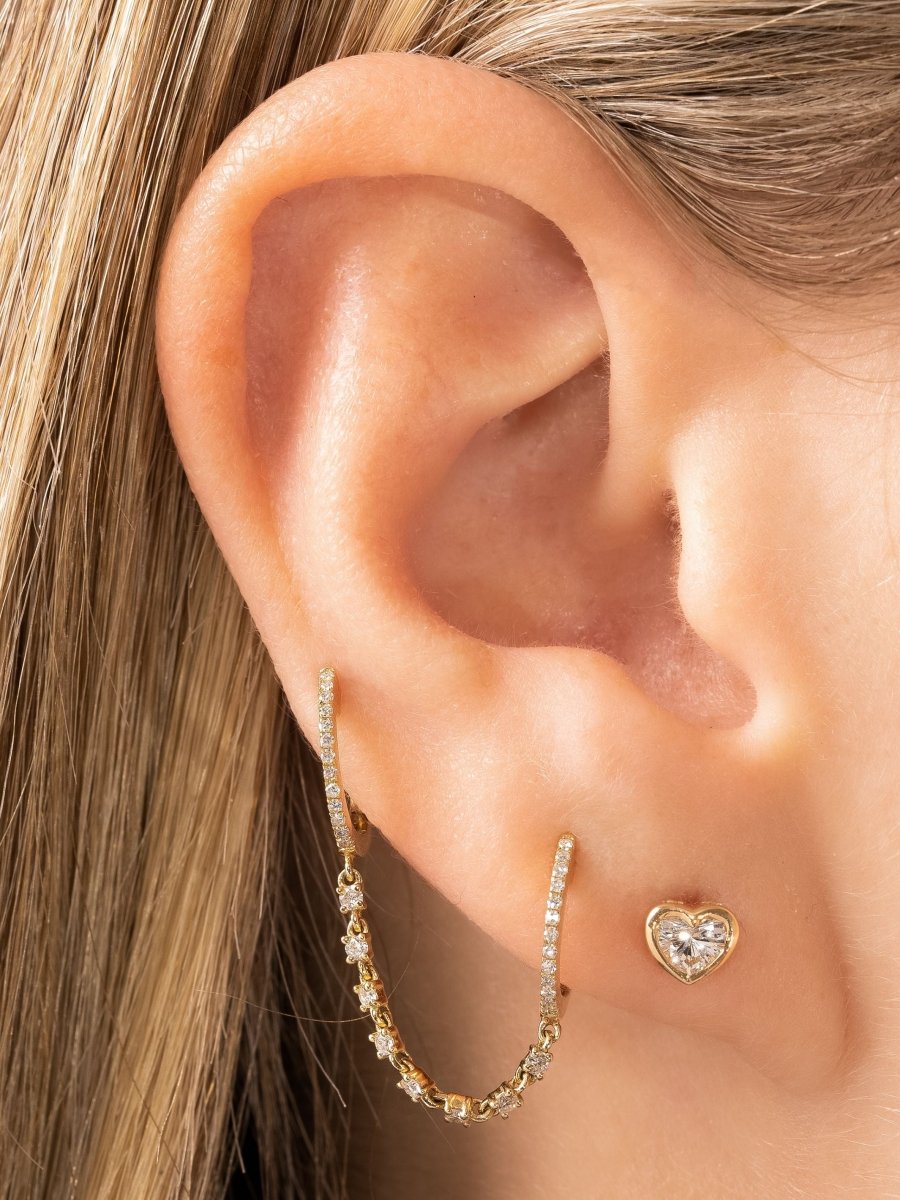 Diamond heart stud earring paired with diamond huggie chain earring on model ear