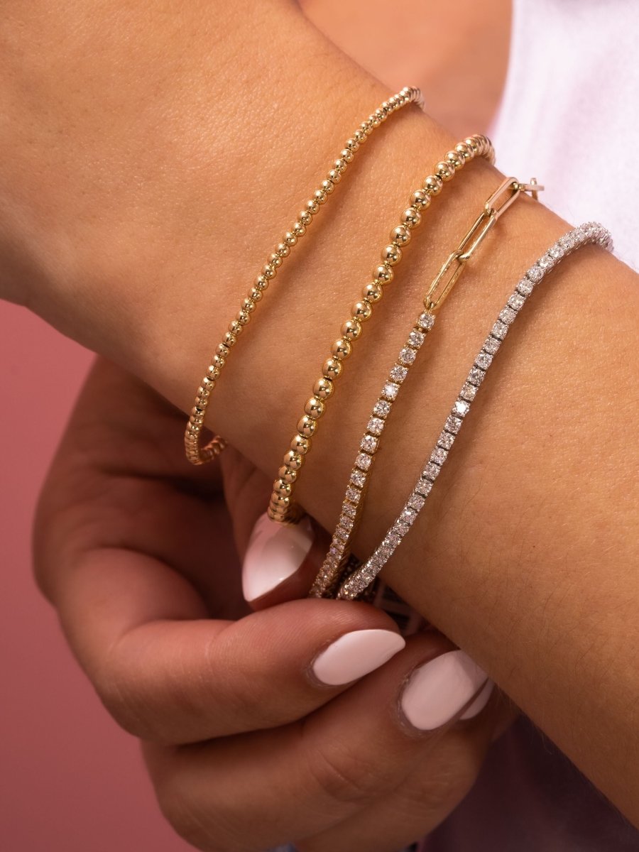 14K gold diamond tennis chain bracelet layered with diamond tennis bracelet and gold beaded bracelets