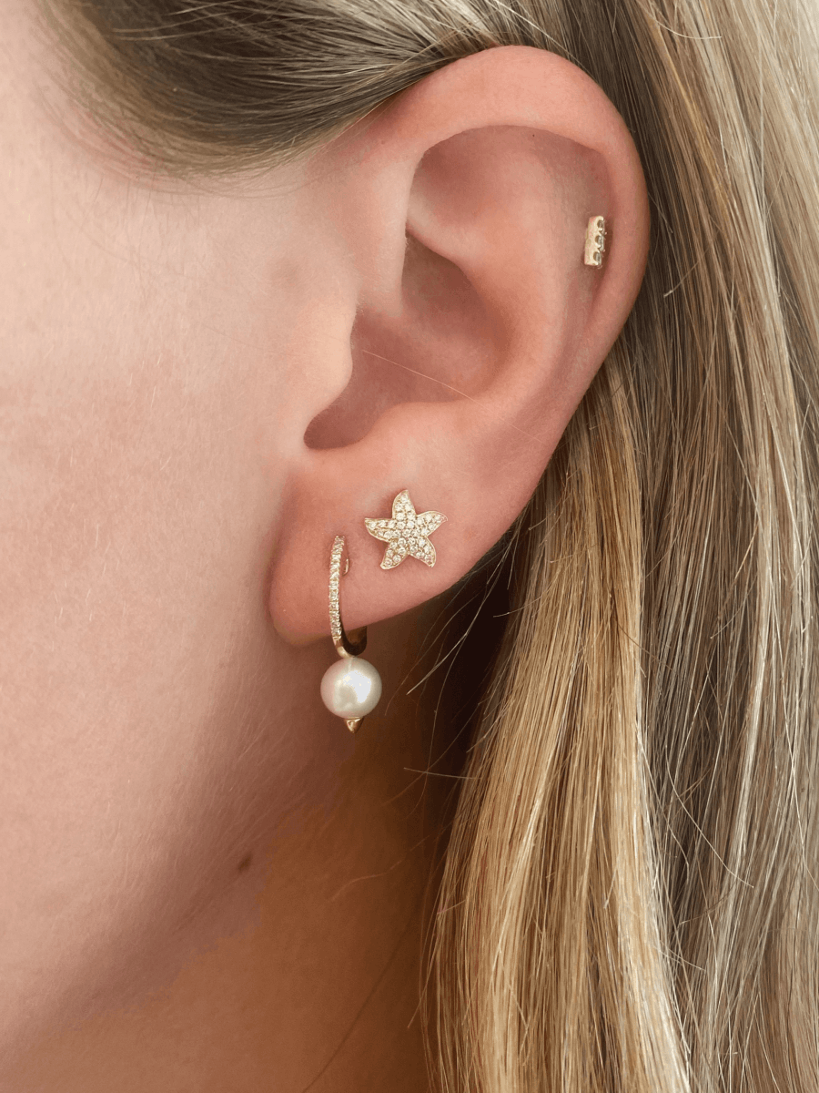Gold starfish earring paired with diamond bar stud and pearl drop huggie with diamonds