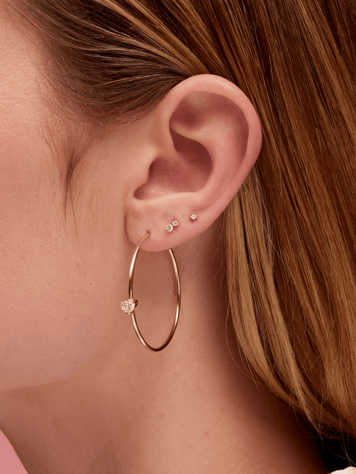 Diamond stud paired with double diamond stud and large gold hoop with heart diamond on model ear