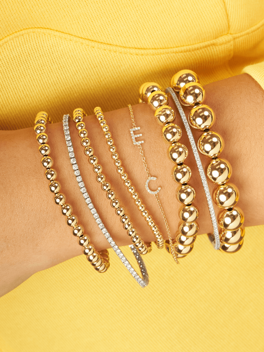 Dainty gold chain bracelet with two pave diamond initials layered with gold beaded bracelets and diamond tennis bracelets 