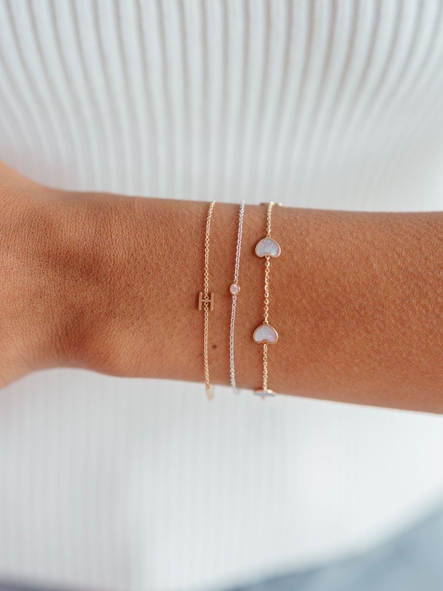 Dainty gold chain bracelet with single initial letter layered with white gold chain bracelet with single diamond and bracelet with mother of pearl hearts on dainty gold chain