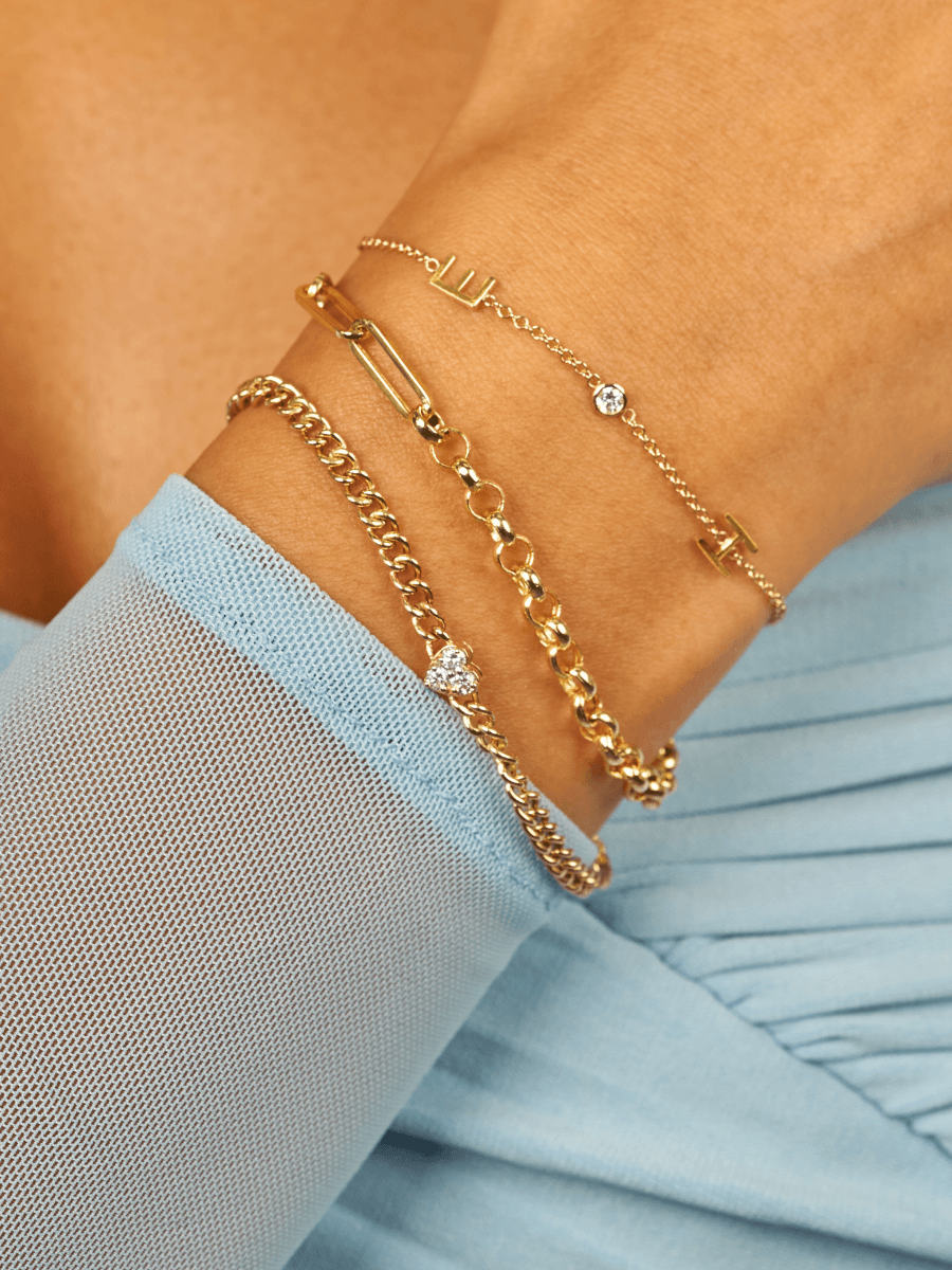 Dainty gold chain with two gold initial letters and singular diamond layered with half rolo chain and half paperclip chain bracelet and and bracelet with diamond heart on thick gold chain