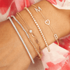 Dainty gold chain bracelet with two diamond initial letters and gold heart layered with diamond tennis bracelets, white and yellow gold beaded bracelet, and singular diamond bracelet half paperclip chain and half small dainty chain