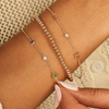Dainty gold chain with two gold initial letters and singular diamond layered with gold beaded bracelet and dainty gold chain bracelet with singular sapphire, diamond, and emerald 