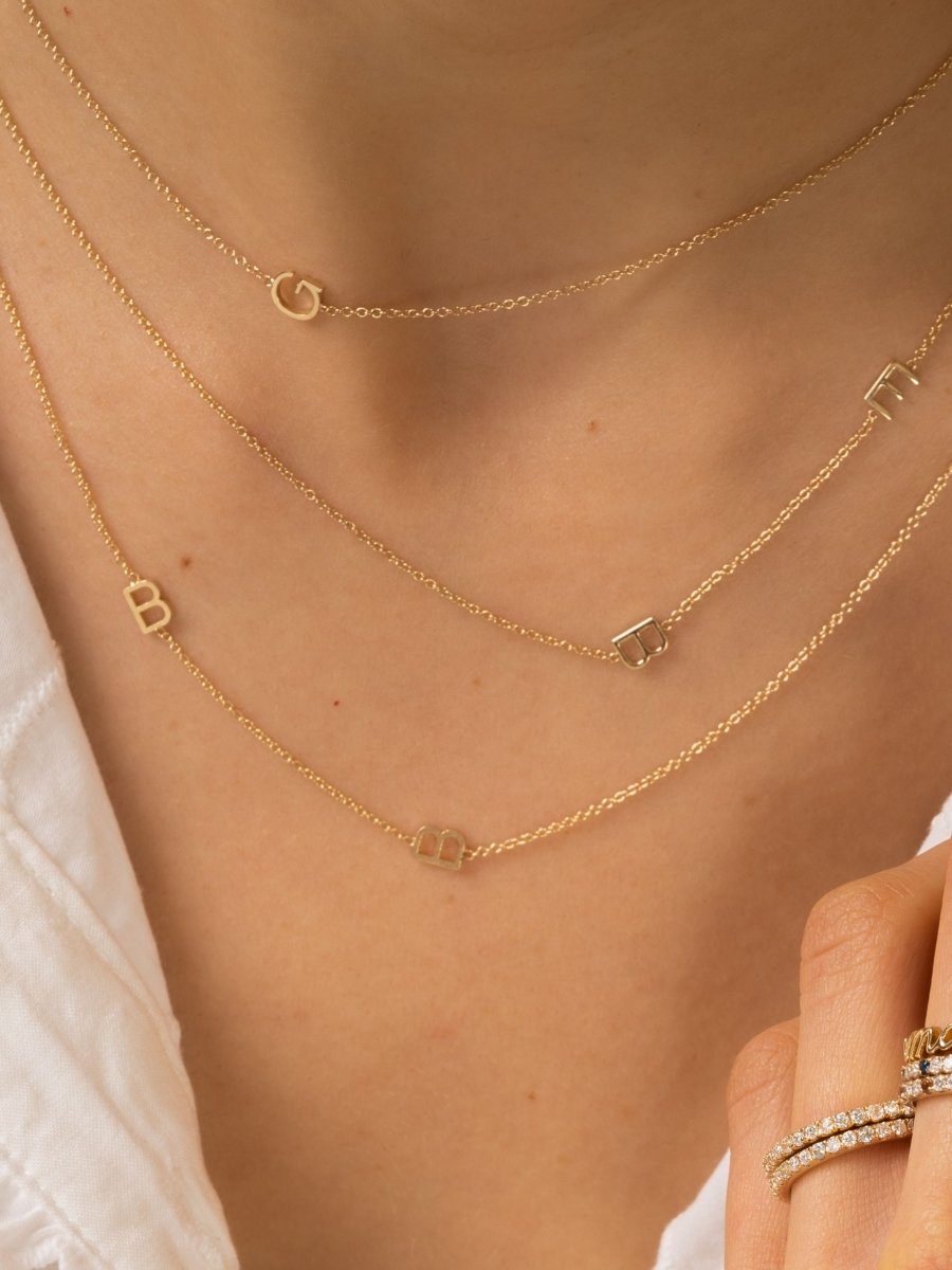 Dainty gold chain with single initial letter layered with two other dainty gold chains with two initial letters