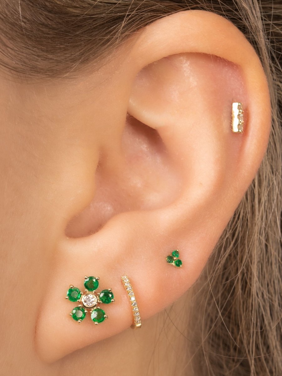Emerald and diamond flower stud paired with diamond huggie, emerald trio stud, and diamond bar stud on model ear