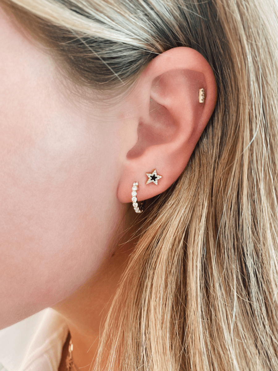 Black star earrings with diamonds paired with diamond bar stud and small diamond hoop on model ear